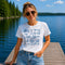 Woman wearing a white t-shirt with blue graphics and text, standing on a dock by a lake.
