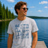 Man wearing a gray t-shirt with blue graphics and text by a lake
