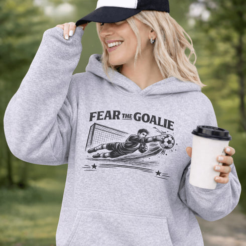 Woman wearing grey hoodie with “Fear The Goalie” soccer goalkeeper design featuring diving goalie making a save