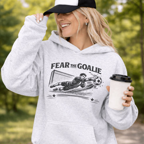 Woman wearing grey hoodie with “Fear The Goalie” soccer goalkeeper design featuring diving goalie making a save