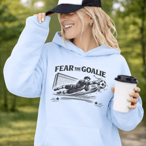 Woman wearing grey hoodie with “Fear The Goalie” soccer goalkeeper design featuring diving goalie making a save