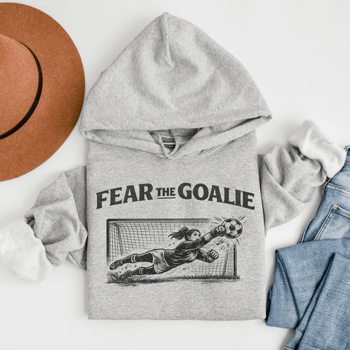 woman wearing grey hoodie with “Fear The Goalie” soccer goalkeeper design featuring diving goalie making a save
