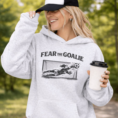 woman wearing grey hoodie with “Fear The Goalie” soccer goalkeeper design featuring diving goalie making a save