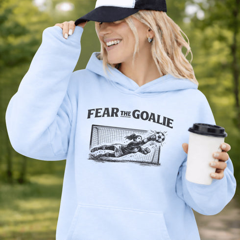woman wearing grey hoodie with “Fear The Goalie” soccer goalkeeper design featuring diving goalie making a save
