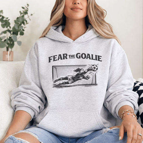 woman wearing grey hoodie with “Fear The Goalie” soccer goalkeeper design featuring diving goalie making a save
