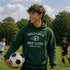 Person wearing a green hoodie with a soccer-themed quote on a soccer field
