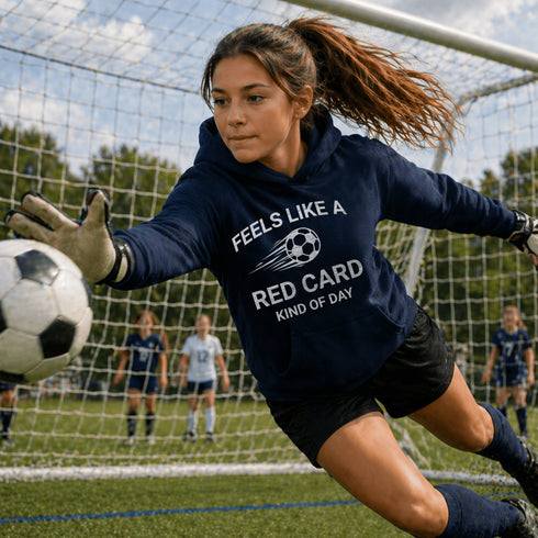 Soccer goalkeeper in action wearing a hoodie with text on a soccer field.