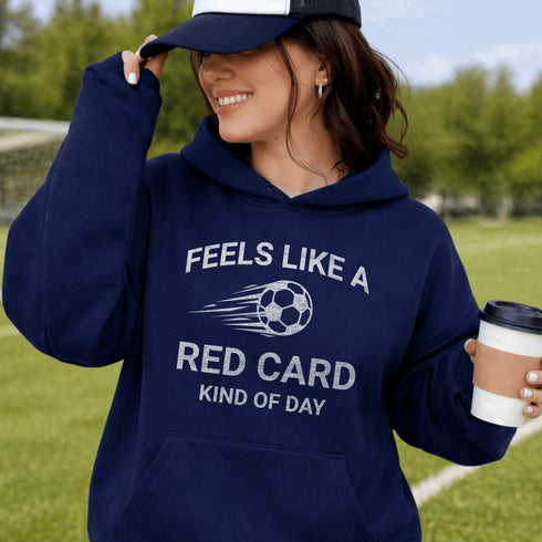 Person wearing a navy hoodie with text and a soccer ball graphic, holding a coffee cup outdoors.