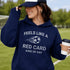 Person wearing a navy hoodie with text and a soccer ball graphic, holding a coffee cup outdoors.