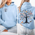 This hoodie features a delightful folk art design of vibrant birds perched in a tree adorned with colorful leaves and blooming flowers, creating a scene that radiates joy and creativity.