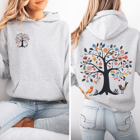 This hoodie features a delightful folk art design of vibrant birds perched in a tree adorned with colorful leaves and blooming flowers, creating a scene that radiates joy and creativity.