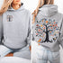 This hoodie features a delightful folk art design of vibrant birds perched in a tree adorned with colorful leaves and blooming flowers, creating a scene that radiates joy and creativity.