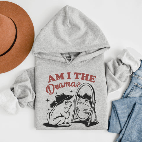 Yeehaw, drama lovers! Meet your new favorite hoodie: a fabulous frog in a cowboy hat, staring into a mirror and asking the ultimate question, "Am I the drama?"