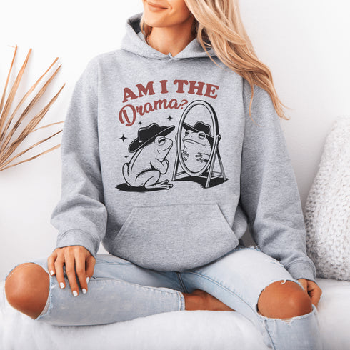 Yeehaw, drama lovers! Meet your new favorite hoodie: a fabulous frog in a cowboy hat, staring into a mirror and asking the ultimate question, "Am I the drama?"