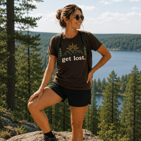 Woman wearing a 'get lost' t-shirt in a scenic outdoor setting with trees and water.