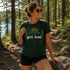Woman hiking in a forest wearing a green t-shirt with 'get lost.' text.
