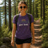 Woman hiking in a forest wearing a purple t-shirt with 'get lost.' text and nature graphics.