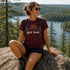 Woman sitting on a rock with a scenic view, wearing a t-shirt with 'get lost' text.