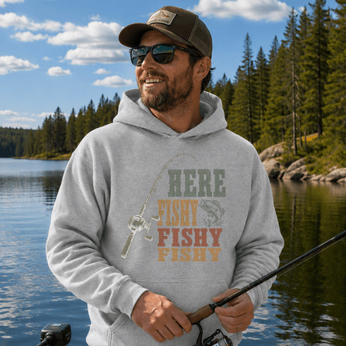 Person wearing a unisex hoodie with a vintage-inspired fishing graphic while holding a fish on a boat surrounded by a scenic lake and forest. Suitable for lifestyle, outdoor, fishing, cabin, camping, and product mockups.