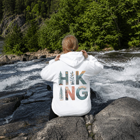 woman wearing hiking hoodie with large nature graphic on back sitting on a rock at the lake
