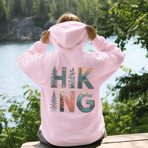 woman wearing hiking hoodie with large nature graphic on back sitting on log in forest