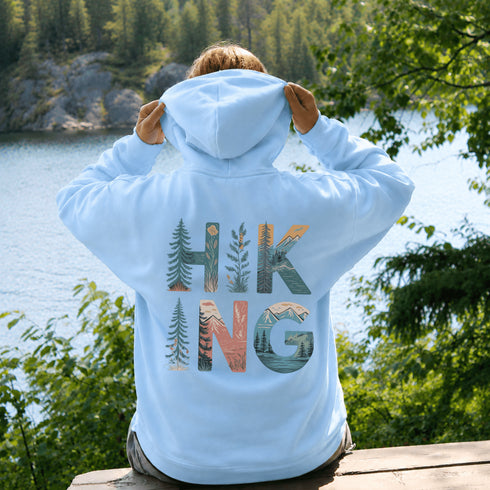woman wearing hiking hoodie with large nature graphic on back sitting on log in forest