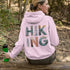 woman wearing hiking hoodie with large nature graphic on back sitting on log in forest