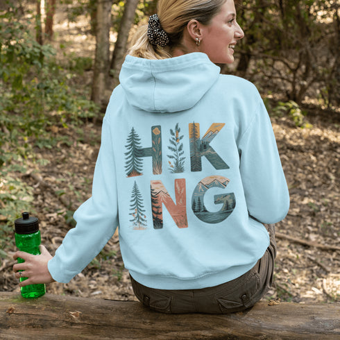 woman wearing hiking hoodie with large nature graphic on back sitting on log in forest