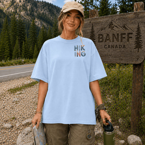 Woman in a light blue t-shirt with 'Hiking' design, standing next to a Banff Canada sign.
