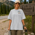 Woman in a hiking shirt standing next to a Banff Canada sign in a mountainous area.