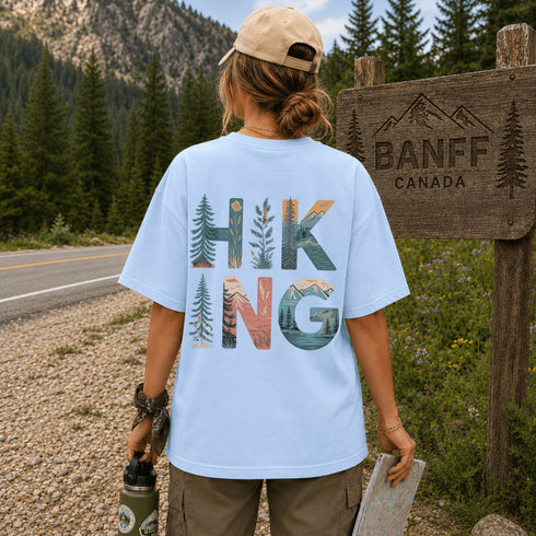 Person wearing a light blue t-shirt with 'HIKING' design, standing near a Banff Canada sign.