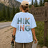 Person wearing a light blue t-shirt with 'HIKING' design, standing near a Banff Canada sign.