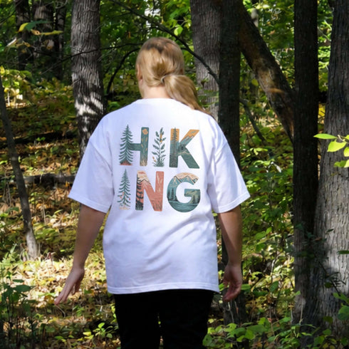 Person wearing a white t-shirt with 'Hiking' design in a forest