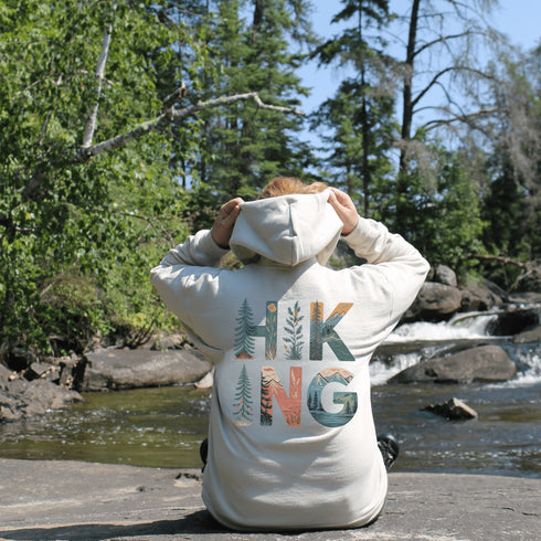 woman wearing hiking hoodie with large nature graphic on back sitting at a waterfall