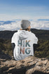 woman wearing hiking hoodie with large nature graphic on back sitting on a mountain