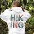 woman wearing hiking hoodie with large nature graphic on back sitting on log in forest