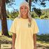 Home Is Out Here Comfort Colors 1717 graphic t-shirt featuring mountain, pine trees, and wilderness artwork with a small left chest logo and large back print.