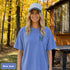 Home Is Out Here Comfort Colors 1717 graphic t-shirt featuring mountain, pine trees, and wilderness artwork with a small left chest logo and large back print.