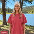 Home Is Out Here Comfort Colors 1717 graphic t-shirt featuring mountain, pine trees, and wilderness artwork with a small left chest logo and large back print.