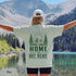 Home Is Out Here Comfort Colors 1717 graphic t-shirt featuring mountain, pine trees, and wilderness artwork with a small left chest logo and large back print.