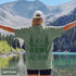 Home Is Out Here Comfort Colors 1717 graphic t-shirt featuring mountain, pine trees, and wilderness artwork with a small left chest logo and large back print.