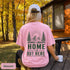 Home Is Out Here Comfort Colors 1717 graphic t-shirt featuring mountain, pine trees, and wilderness artwork with a small left chest logo and large back print.