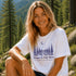 Woman wearing a white t-shirt with a nature-themed design in a forest setting