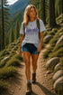 Woman hiking in a forested area wearing a t-shirt with nature-themed design.
