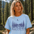 Woman wearing a light blue t-shirt with a nature graphic and text in a forest setting