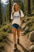 Woman hiking on a trail in a forest wearing a t-shirt with a nature-themed design.
