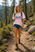 Woman hiking on a trail in a forest wearing a pink t-shirt with a nature design.