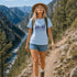 Woman hiking on a mountain trail with a scenic view of a river and mountains.