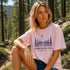Woman sitting outdoors wearing a pink t-shirt with nature-themed design.