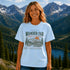 Woman wearing Wander Far Take the Scenic Route mountain hiking graphic t-shirt featuring vintage mountain landscape artwork with pine trees and sunset background.